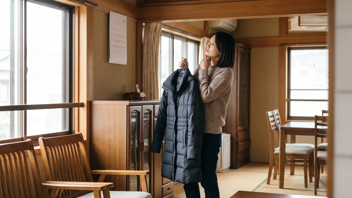 日本の住宅で壁のカレンダーを見ながら、ダウンコートを手に預ける時期と戻る時期を考えている女性の写真