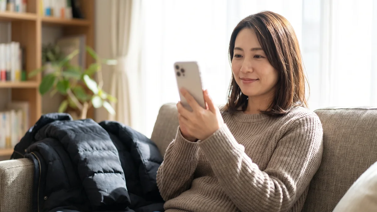 ソファでスマートフォンの口コミを読む日本人女性（イメージ）