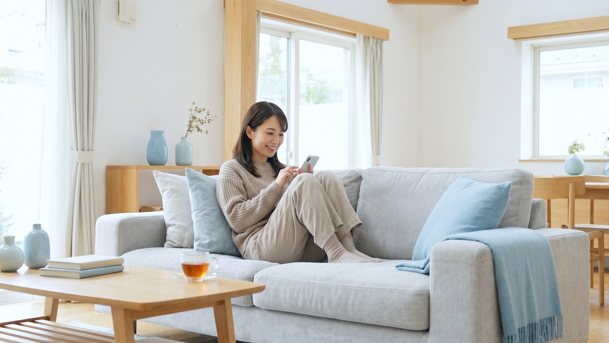 ソファでスマートフォンの口コミを読む日本人女性